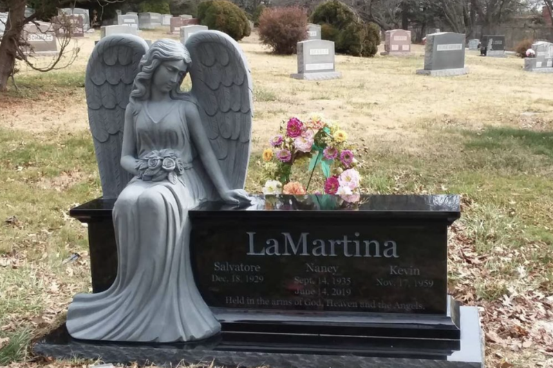 Angel statue memorial bench with black granite base in a peaceful cemetery setting