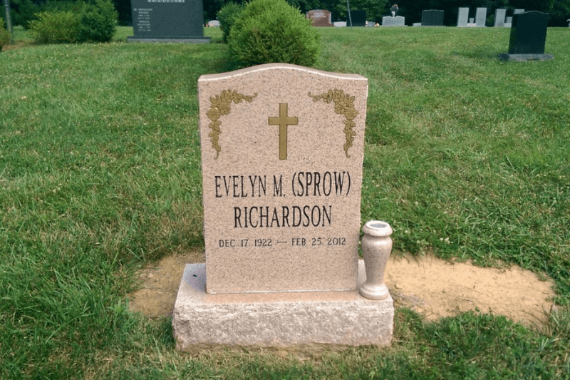 Granite religious headstone with a cross, floral details, engraved name, dates, and vase