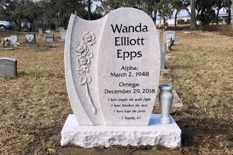 Light-colored granite headstone with carved roses, engraved lettering, and a matching flower vase