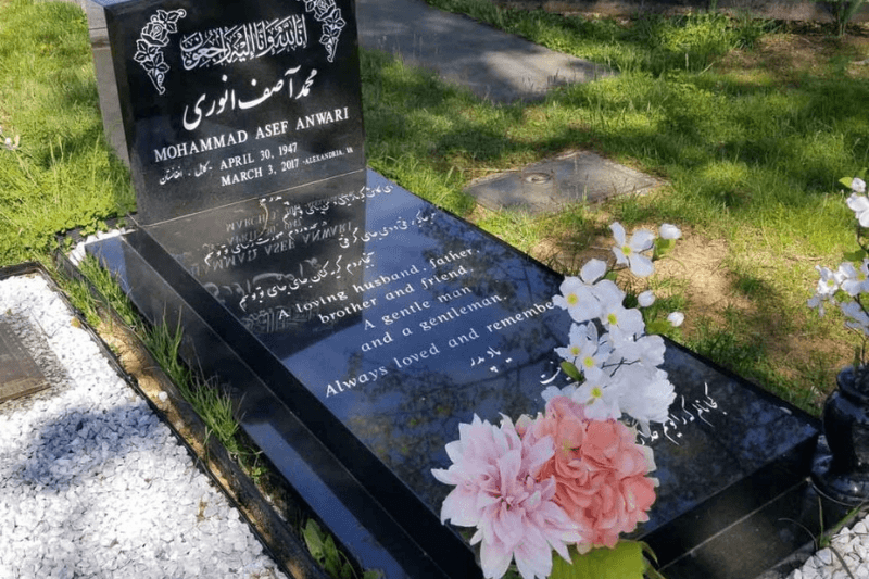 Polished black upright headstone with ledger-style grave marker and flowers