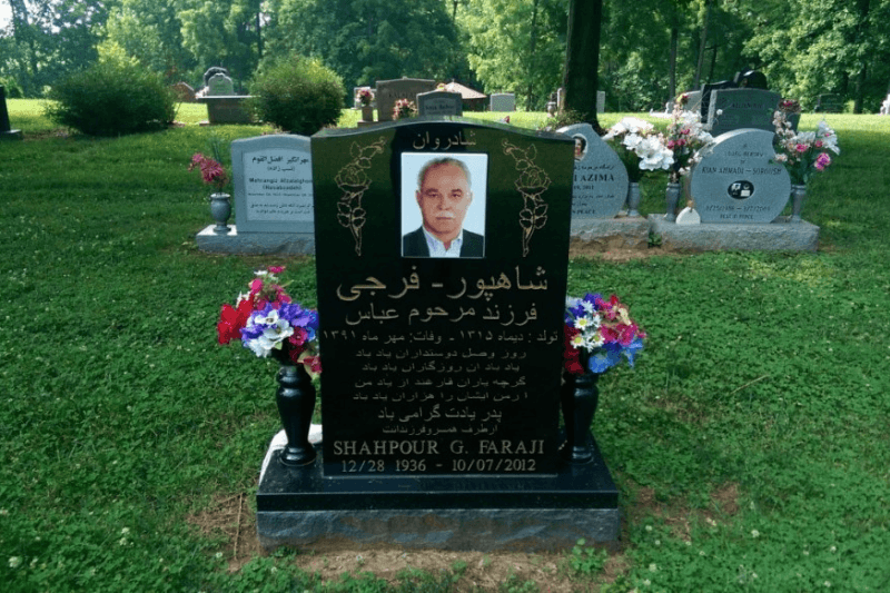 Upright black granite memorial with gold lettering, a central portrait, flowers, and matching vases