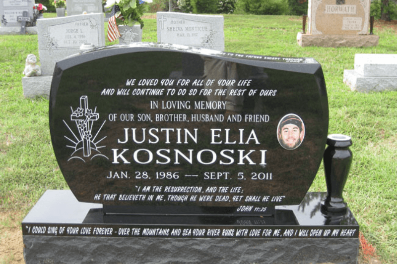 Wide polished black granite headstone with engraved artwork, a portrait, and a decorative side vase