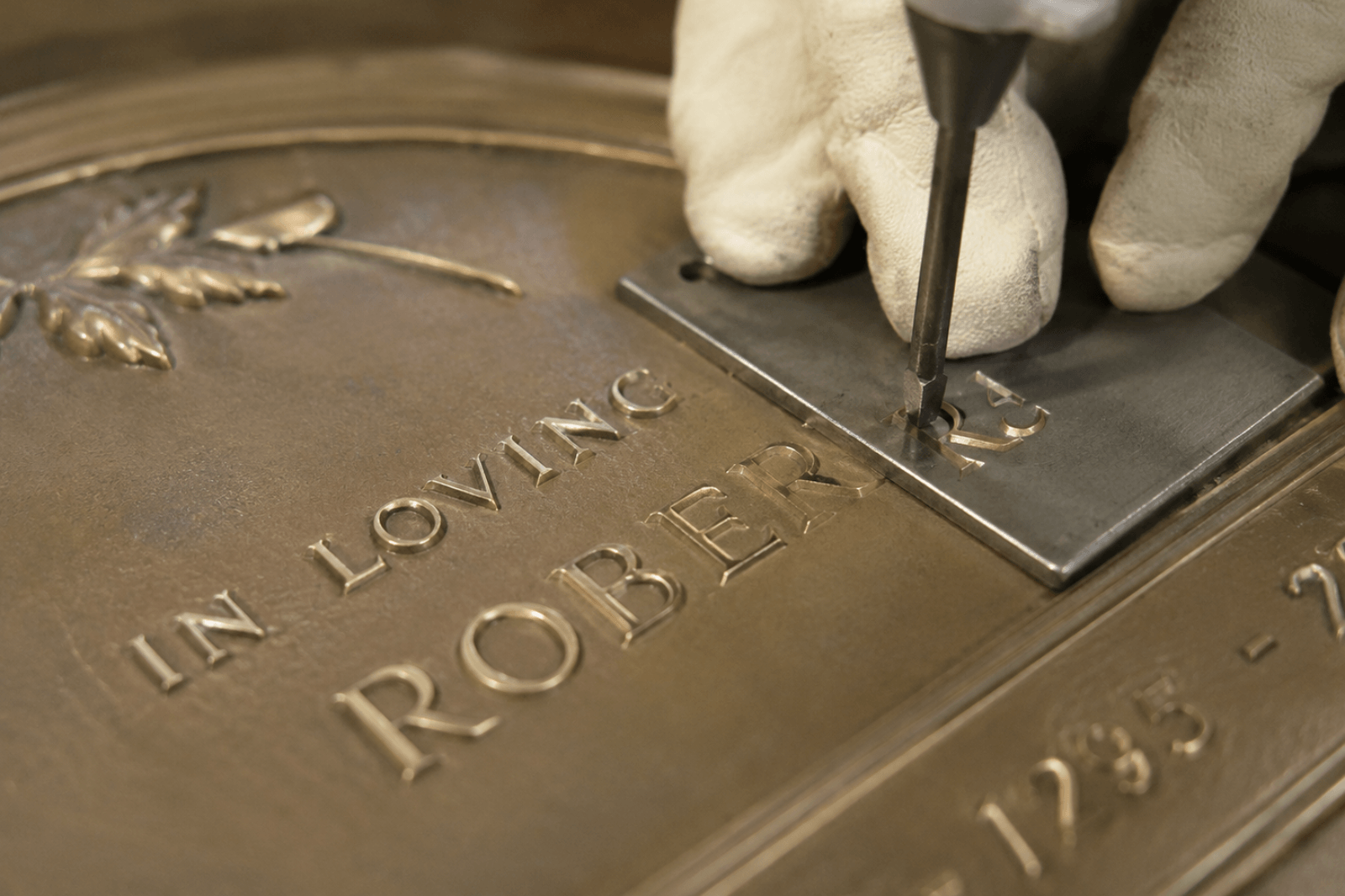 Craftsperson hand engraving lettering on a bronze memorial plaque